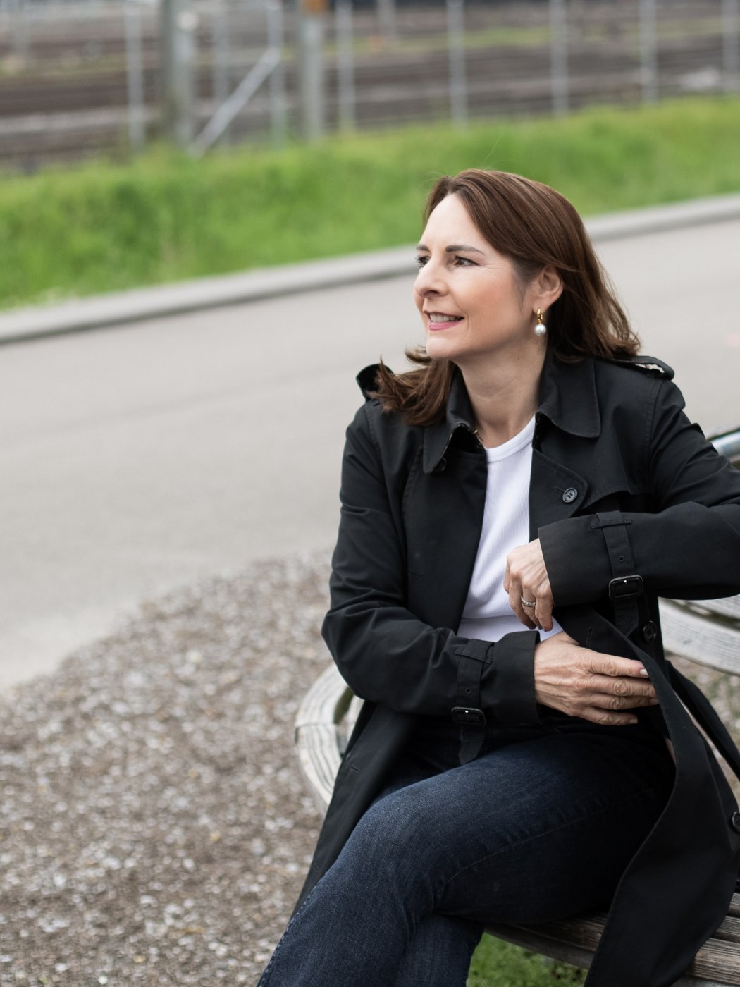 Liliane sitzt auf einer Bank mit Bahngleisen im Hintergrund